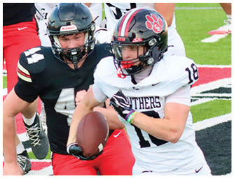 Two people in football uniforms are actively playing on a field with one person holding the ball and the other attempting to catch or tackle. Description generated by AI