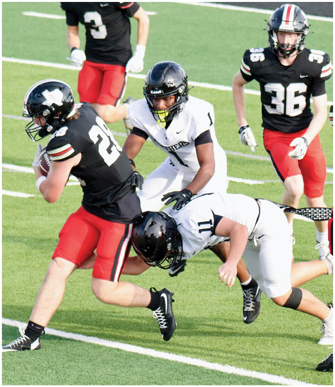 Several people wearing football helmets and uniforms are actively engaged in a play on a green field, with some running and one person appearing to tackle another. Description generated by AI
