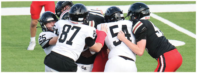 Several people wearing football uniforms are engaged in a close physical play on a grassy field. Description generated by AI