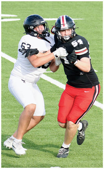 Two people wearing football helmets and uniforms are engaged in a physical struggle on a grassy field. Description generated by AI