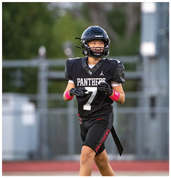 A person wearing a black football helmet and a black jersey with the word Panthers is standing outdoors, looking to the side. Description generated by AI