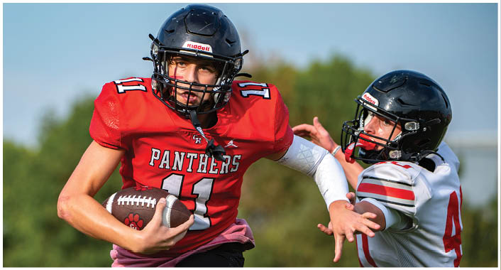 A person wearing a black football helmet and red jersey with the number 11 is looking intently forward outdoors with a blurred green background. Description generated by AI