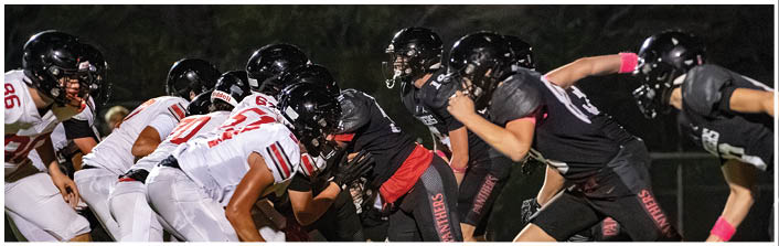 Two teams of football players in black and white uniforms are lined up facing each other on a field, preparing for a play. Description generated by AI