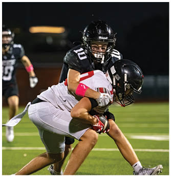 Two people in football uniforms are engaged in a tackle on a grassy field during a nighttime game. Description generated by AI