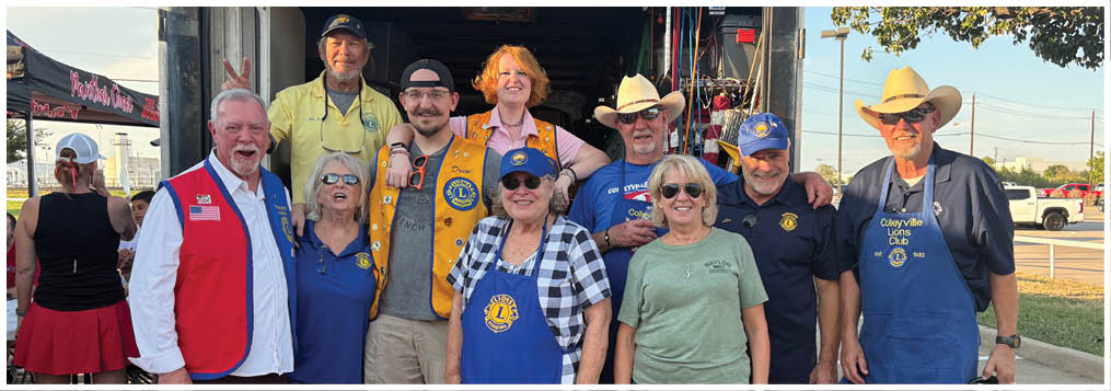 A group of people wearing casual clothing and aprons stand together outdoors on a paved surface. Description generated by AI
