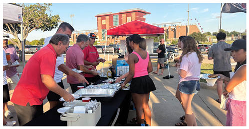 People in casual clothing are serving themselves food from a buffet table outdoors. Description generated by AI