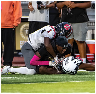 Two people in football uniforms are on the field with one person tackling the other who is holding the ball. Description generated by AI