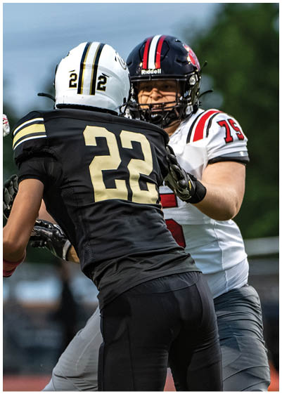 Two people wearing football uniforms and helmets are engaged in a play on a field with one person in a white jersey and the other in a black jersey. Description generated by AI