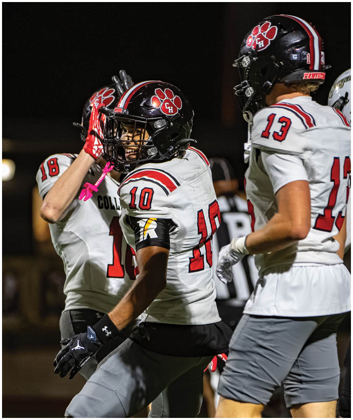 Several people wearing football uniforms with helmets are on a field at night, appearing to celebrate or communicate during a game. Description generated by AI