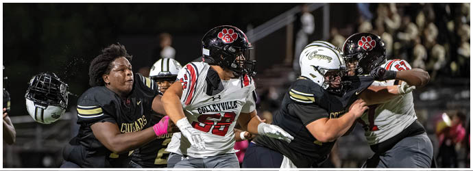 Several people in football uniforms are engaged in a dynamic play on a field during a game at night. Description generated by AI