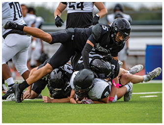 Several people wearing football helmets and uniforms are piled on the ground during a game on a grassy field. Description generated by AI