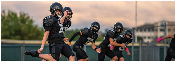 Several people wearing football helmets and uniforms are standing outdoors under a cloudy sky. Description generated by AI