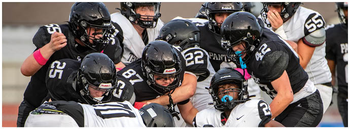 A group of people wearing black and white football uniforms are engaged in a close huddle on a field during a game. Description generated by AI