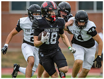 A person in a black football uniform with the word Panthers is running with the ball while being chased by three people in white and black uniforms on a sports field. Description generated by AI