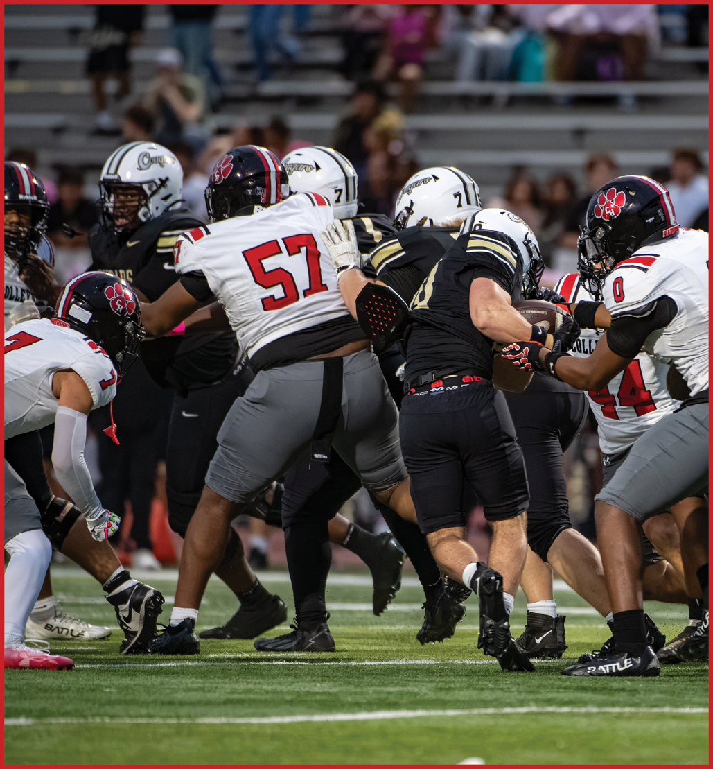 People in football uniforms are engaged in a play on the field with one person holding the ball while others attempt to block or tackle. Description generated by AI