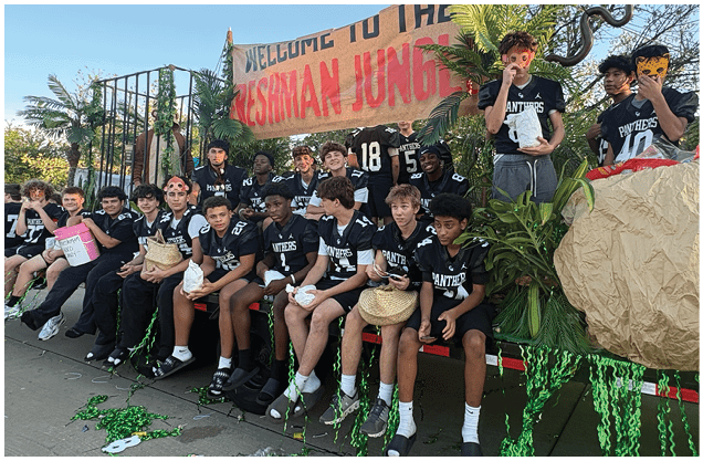 A group of people wearing matching sports jerseys are sitting on a bench outdoors with green streamers scattered on the ground in front of them. Description generated by AI
