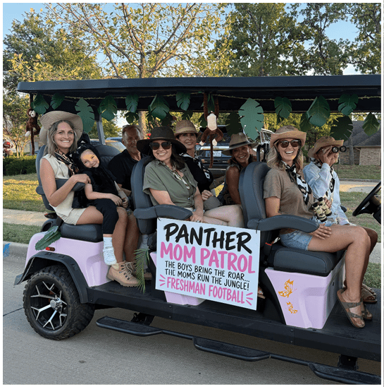 A group of people wearing hats and casual clothing are sitting and smiling on a decorated golf cart with a sign that reads “Panther Mom Pool" and references football and family roles. Description generated by AI