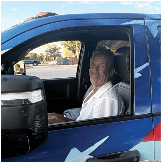 A person wearing a white shirt is sitting inside a vehicle with a colorful exterior featuring a blue, red, and white design. Description generated by AI