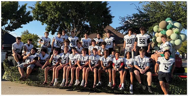 People wearing white sports jerseys with black trim are sitting closely together. Description generated by AI