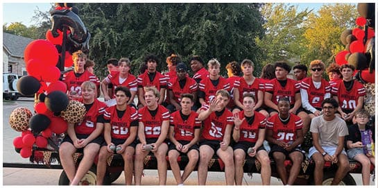 People wearing red sports jerseys with white stripes are standing close together outdoors. Description generated by AI
