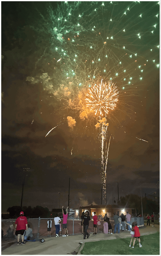 Fireworks burst in the night sky above a crowd of people watching from a waterfront area. Description generated by AI