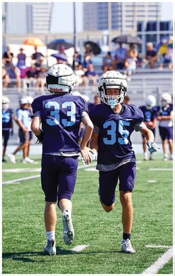 Three football players in blue and white uniforms running on a field. Description generated by AI