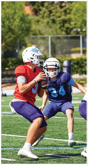Three football players in blue and white uniforms running on a field. Description generated by AI