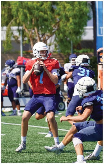 Three football players in blue and white uniforms running on a field. Description generated by AI