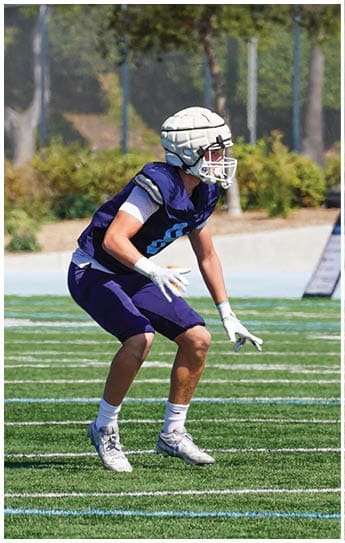 Three football players in blue and white uniforms running on a field. Description generated by AI