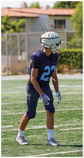 Three football players in blue and white uniforms running on a field. Description generated by AI