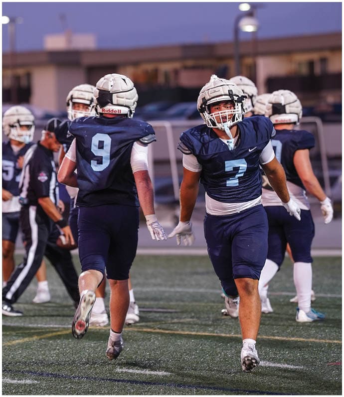 Three football players in blue and white uniforms running on a field. Description generated by AI