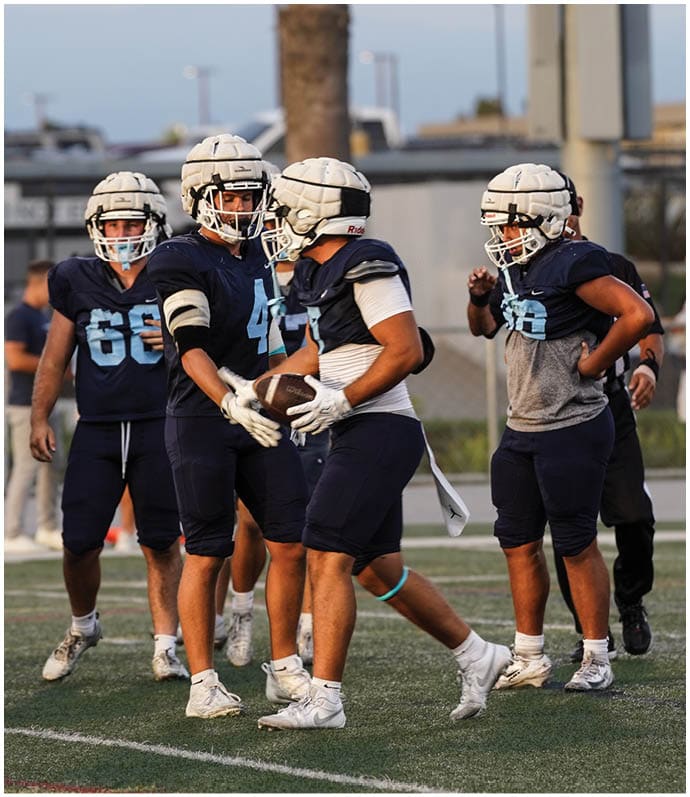 Three football players in blue and white uniforms running on a field. Description generated by AI