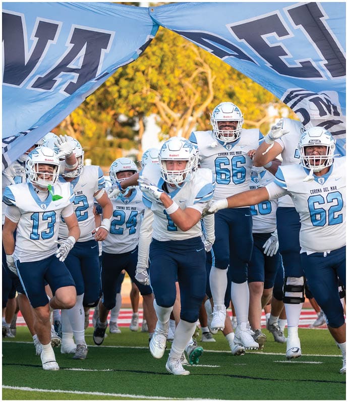 Three football players in blue and white uniforms running on a field. Description generated by AI