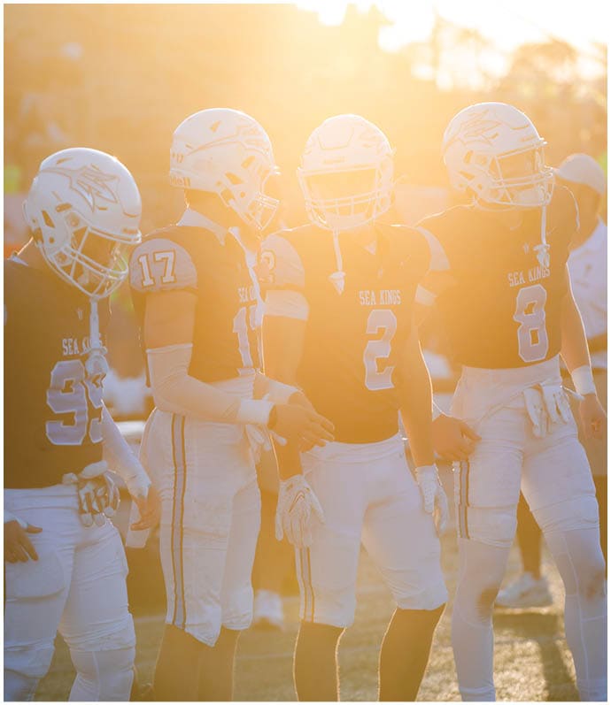 Three football players in blue and white uniforms running on a field. Description generated by AI