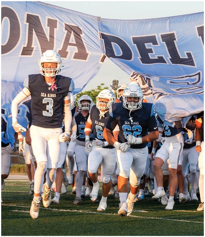 Three football players in blue and white uniforms running on a field. Description generated by AI