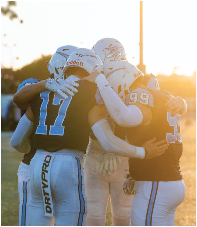 Three football players in blue and white uniforms running on a field. Description generated by AI