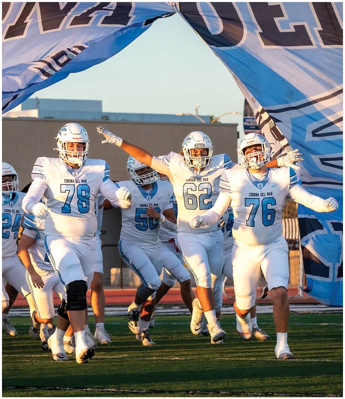 Three football players in blue and white uniforms running on a field. Description generated by AI