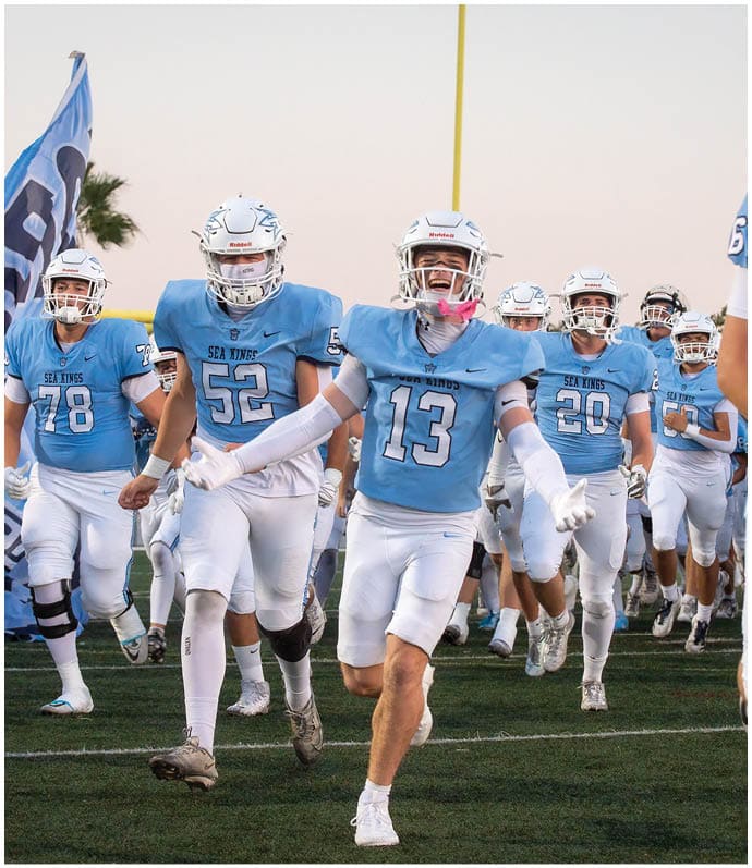 Three football players in blue and white uniforms running on a field. Description generated by AI