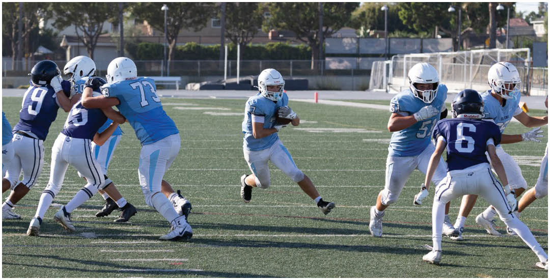 Three football players in blue and white uniforms running on a field. Description generated by AI