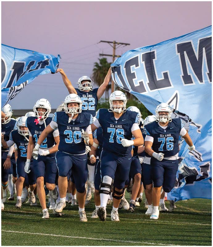 Three football players in blue and white uniforms running on a field. Description generated by AI