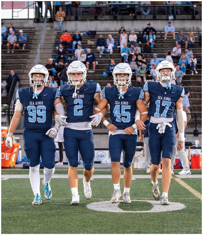 Three football players in blue and white uniforms running on a field. Description generated by AI