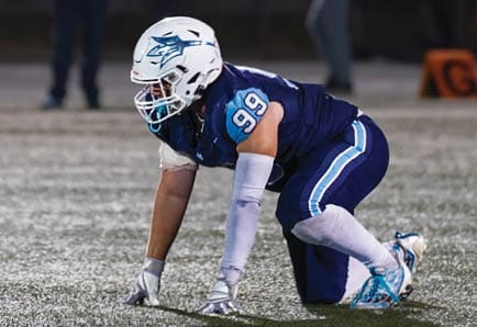 Two adults in football uniforms are actively engaged in a play on a field, with one holding the ball and the other preparing to tackle. Description generated by AI