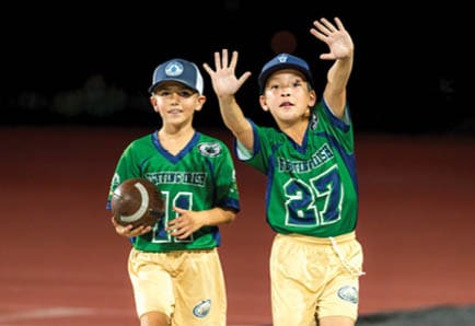 People in sports uniforms are running on a field with one person holding a football while others chase behind. Description generated by AI