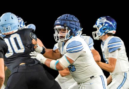 Four people in football uniforms are positioned on a field, appearing ready to start a play during a game. Description generated by AI