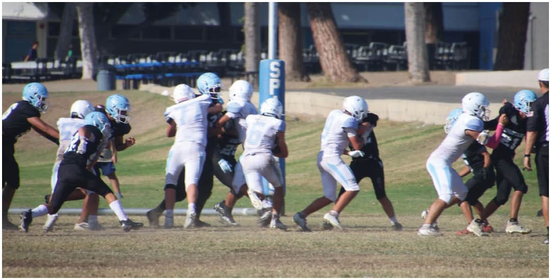 Three football players in blue and white uniforms running on a field. Description generated by AI