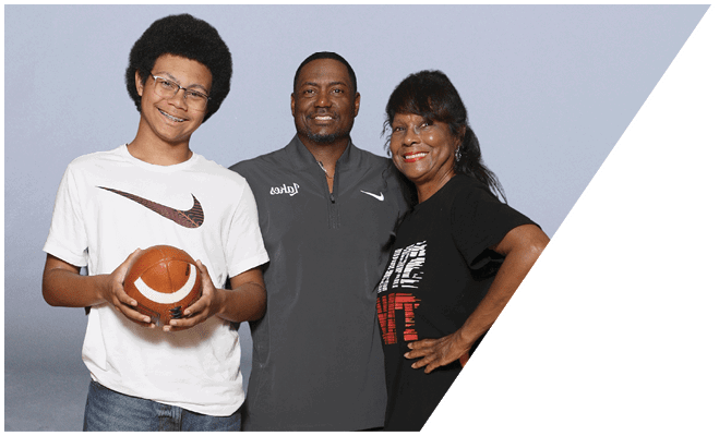 Three people stand closely together smiling, with one holding a football, against a plain light background. Description generated by AI