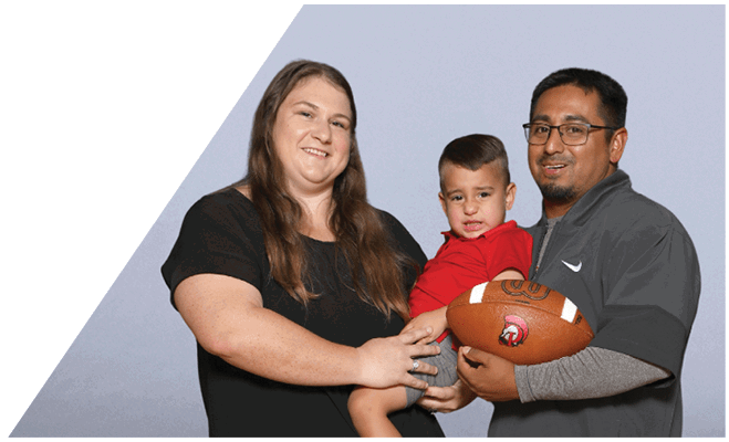 Two adults holding a child who is holding a football, all smiling against a plain background. Description generated by AI