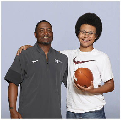 Two people stand side by side smiling, with one person holding a basketball and the other wearing a dark sports shirt with the word “Lakes" on it. Description generated by AI