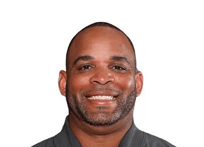 A smiling person with short hair and a trimmed beard wearing a dark collared shirt against a white background. Description generated by AI