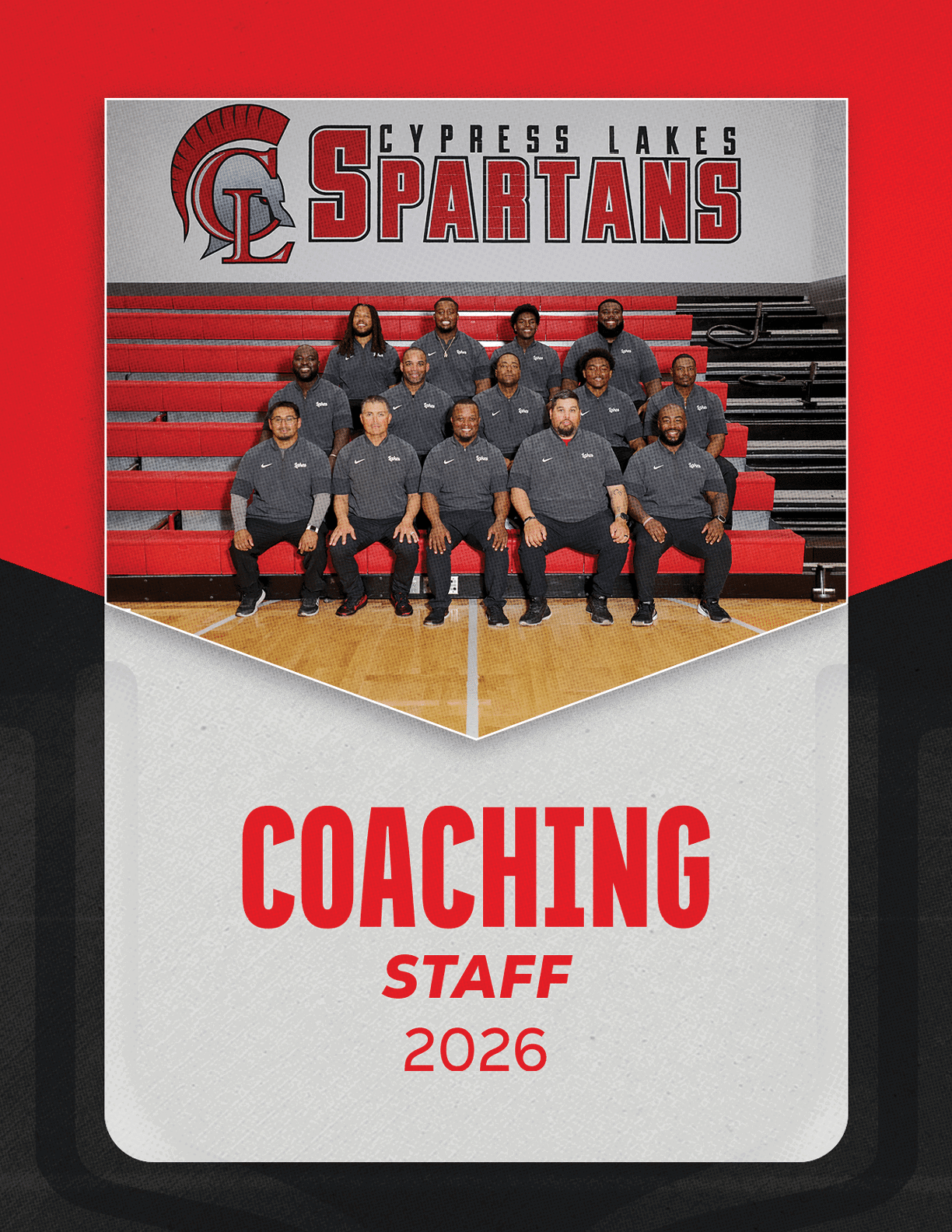 A group of adults wearing matching dark gray polo shirts pose seated and standing on red bleachers inside a gymnasium under a banner that reads Cypress Lakes Spartans with a Spartan helmet logo, with the text coaching staff 2026 below. Description generated by AI